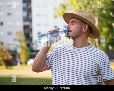 Jeune homme buvant de l'eau dans le parc par une journée d'été ensoleillée. Banque D'Images