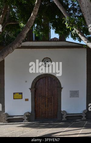 Fataga, Espagne - 17 août 2026 : Vue architecturale de l'église San Jose avec des bancs en pierre et une horloge montée sur un mur blanc à San Bartolome de Banque D'Images