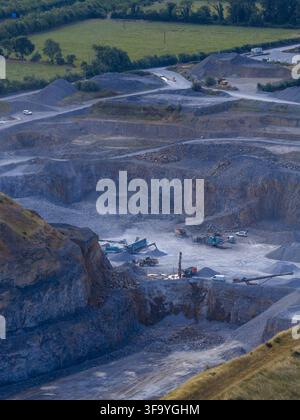Vue aérienne d'une carrière à ciel ouvert active avec des engins de chantier lourds, des excavatrices et des tas de pierre concassée entourés de champs verts à Drogheda, comté de L Banque D'Images