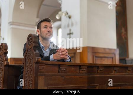 Un homme agenouille tranquillement dans une église catholique européenne pendant la messe solennelle. Il montre une foi profonde et participe au culte. Banque D'Images