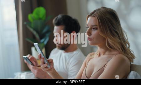 Couple familial caucasien accro aux gadgets se réveillant le matin en utilisant des téléphones portables assis au lit en tapant des messages avec une addiction aux smartphones séparés Banque D'Images