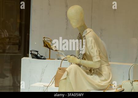 Mannequin d'été Vitrine Boutique Prada rue. Vitrine de magasin de mode avec mannequin féminin en robe crème, sac à main beige et sandales de luxe. Milan, Italie - 24 juin 2026 Banque D'Images