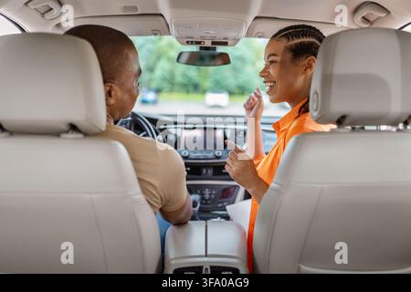 Jeune couple afro-américain joyeux dans une voiture, discutant et riant Banque D'Images