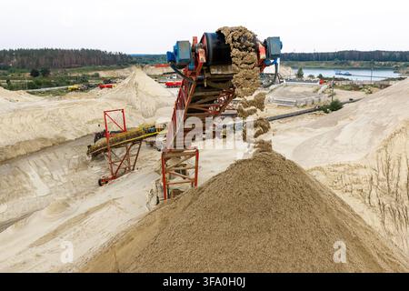 Vue aérienne d'une carrière de sable avec un tapis roulant transportant le sable en grands tas dans une carrière industrielle en Pologne. Banque D'Images