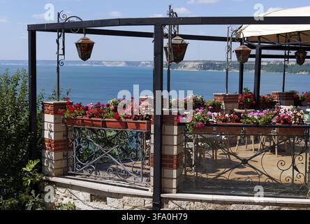 Espace de repas extérieur sur une terrasse avec des fleurs colorées, profitant de vues panoramiques sur la mer et le paysage côtier lointain. Bulgarie, Kaliakra, 16 août Banque D'Images