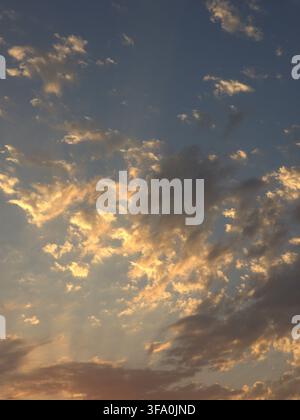 Les nuages dorés du coucher de soleil brillent contre un ciel bleu profond. La lumière du soleil perce à travers les couches de nuages dispersées. Des tons chauds éclairent les bords du ciel. Les formations nuageuses kre Banque D'Images