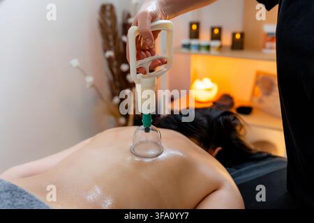 Thérapeute effectuant un massage par thérapie par ventouses sur le dos d'une femme dans une clinique d'ostéopathie chaude, utilisant une ventouse pour soutenir le soulagement musculaire, la relaxation, un Banque D'Images