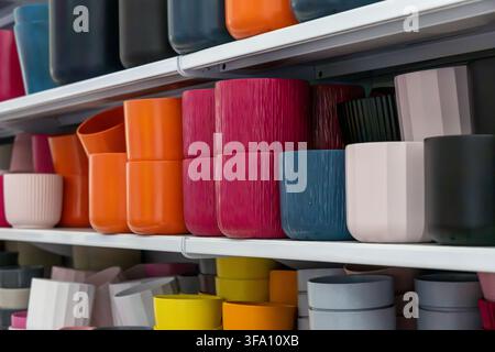 Un assortiment éclatant de pots de fleurs en céramique et en plastique de différentes tailles et teintes est soigneusement disposé sur des étagères blanches Banque D'Images