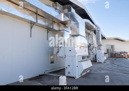 De grandes unités de climatisation industrielles blanches sont connectées à des systèmes de conduits métalliques étendus montés sur le mur extérieur d'un bâtiment moderne Banque D'Images