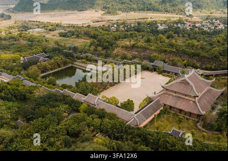 Vue par drone de la pagode de Bai Dinh à Ninh Binh, au Vietnam, montrant des toits de temples traditionnels, de vastes cours, un étang et une campagne luxuriante entourée de Banque D'Images