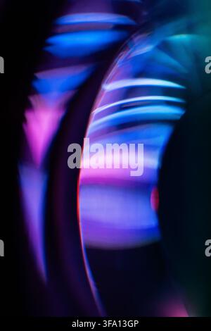 Traînées de lumière néon bleu, violet et rose abstraites se réfractent à travers une lentille en verre incurvée, créant un arrière-plan futuriste lumineux avec un flou de mouvement doux Banque D'Images
