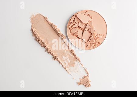 Vue de dessus d'une recharge de poudre compacte pêche craquée à côté d'un large échantillon cosmétique et de poussière de maquillage dispersée sur un fond blanc propre pour les produits de beauté Banque D'Images