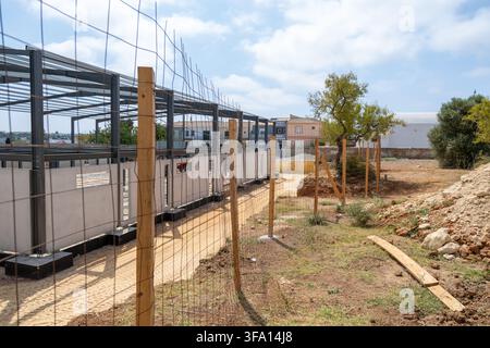 Une nouvelle structure en acier est en train d'être érigée sur un chantier de construction avec des panneaux muraux en béton et une clôture temporaire entourant la zone Banque D'Images