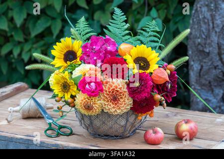 Arrangement floral avec des dahlias rouges et orange, des tournesols, des fleurs d'hortensia, une rose, des physalis, des baies de rowan, des graminées et des feuilles de fougère dans un panier Banque D'Images