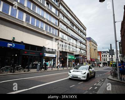 Dublin, Irlande – 22 mai 2026 : Scène de rue urbaine à Dublin avec un taxi, des piétons, des boutiques et une architecture de bureau du milieu du siècle. Banque D'Images