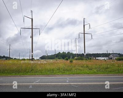 Plusieurs poteaux électriques se dressent dans un champ avec des lignes électriques qui passent au-dessus, tandis qu'une maison est visible en arrière-plan. Banque D'Images
