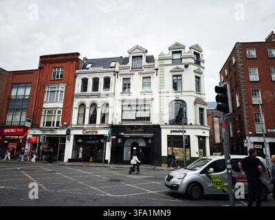 Dublin, Irlande – 22 mai 2026 : Rue animée de Dublin avec des façades victoriennes historiques, des magasins, un taxi et des piétons à une intersection. Banque D'Images