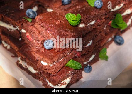Close-up de carrés de brownie au chocolat riche avec des couches crémeuses et à la fraise, garnis de myrtilles et de menthe. Dessert fait maison appétissant avec un Banque D'Images