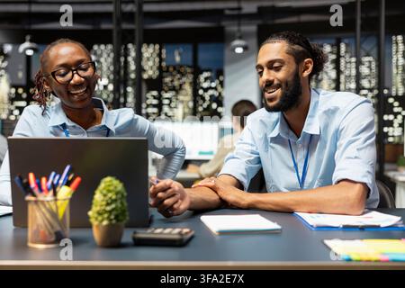 Des employés heureux s'amusent en discutant des idées de projet dans un espace de coworking détendu. Des collègues multethniques joyeux profitent d'une conversation agréable au bureau, collaborant pour terminer les tâches de travail Banque D'Images