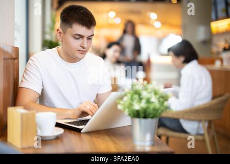Jeune homme assis dans un café et travaillant sur ordinateur portable Banque D'Images