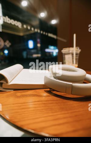 Tokyo, Japon – Scène de café confortable avec livre ouvert, écouteurs blancs et boisson glacée sur table en bois à Banque D'Images