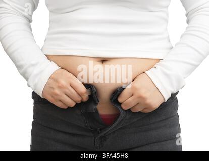 Close-up d'une femme luttant pour enfiler un jean serré à cause d'une prise de poids. Ventre féminin en surpoids contre un fond blanc Banque D'Images
