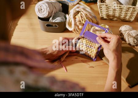 Mains d'une femme utilisant un petit métier à tisser violet dans un atelier d'artisanat Banque D'Images