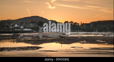 Les bateaux amarrés reposent sur les bancs de sable boueux de l'estuaire de Conwy à marée basse lors d'un coucher de soleil doré sous le mont Conwy dans le nord du Pays de Galles. Banque D'Images