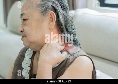 Problème de douleurs musculaires du corps raides, souffrance d'une femme asiatique âgée douloureuse, tenant des douleurs au cou ou massant en frottant le corps, blessure douloureuse assise sur le canapé à la maison. Banque D'Images