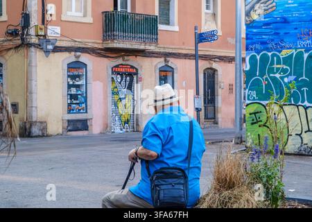 Barcelone – Espagne – 1er août 2026 : Senior assis dans la rue du quartier de Barceloneta, chemise bleue et chapeau de paille, vue arrière, boutique traditionnelle Banque D'Images