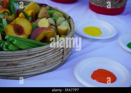 Panier de fruits et légumes coupés accompagnés de peintures colorées sur des assiettes, préparés pour une activité artistique d'estampage pour enfants. Banque D'Images