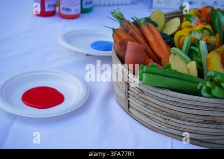 Panier de fruits et légumes coupés accompagnés de peintures colorées sur des assiettes, préparés pour une activité artistique d'estampage pour enfants. Banque D'Images