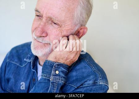Homme âgé ressentant des douleurs d'oreille ou des problèmes auditifs, concept de soins de santé et de bien-être pour les personnes âgées. Vieillesse et inconfort, un portrait rapproché d'un homme âgé Banque D'Images