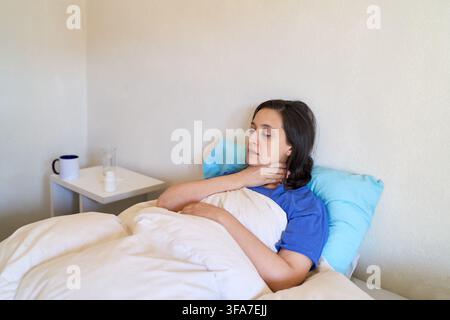 Femme souffrant d'une gorge enflammée et de fièvre reposant au lit, rétablissement à domicile et automédication pour la maladie, concept de santé et bien-être. Patient adulte se sent Banque D'Images