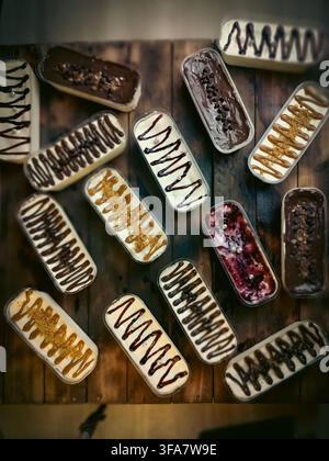 Assortiment de cheesecuits dans un emballage en plastique avec des garnitures au chocolat, aux fruits rouges et au caramel sur une table en bois. Photographie alimentaire idéale pour les desserts et les boulangeries. Banque D'Images