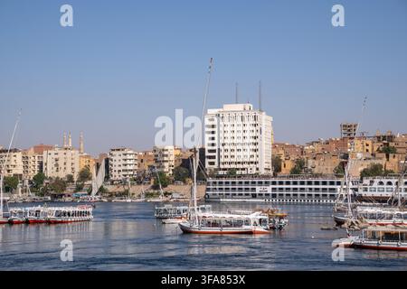 Aswan, Égypte – 10 mars 2026 : felouques et navires de croisière naviguant sur le Nil le long du front de mer d'Aswan depuis Louxor Banque D'Images