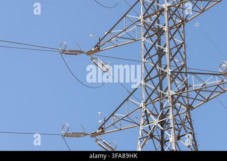 Vue rapprochée d'un grand pylône électrique en métal avec des câbles épais et des isolateurs sous un ciel clair et sans nuages Banque D'Images