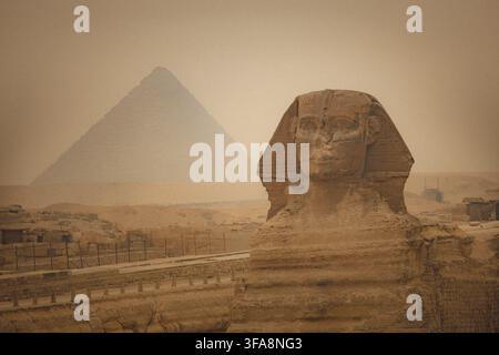 Sphynx devant le fond des Grandes Pyramides égyptiennes. Afrique, plateau de Giza. Une tempête de sable dans l'air donnant un aspect orangé à l'atmosphère. Banque D'Images