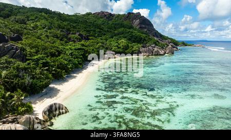 Les eaux turquoise s'écrasent contre les rivages rocheux en contrebas des collines vertes et denses. La Digue, Seychelles. Banque D'Images