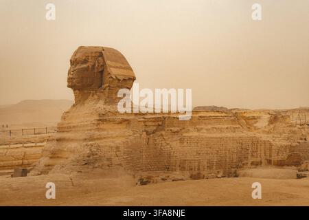 Sphynx devant le fond des Grandes Pyramides égyptiennes. Afrique, plateau de Giza. Une tempête de sable dans l'air donnant un aspect orangé à l'atmosphère. Banque D'Images