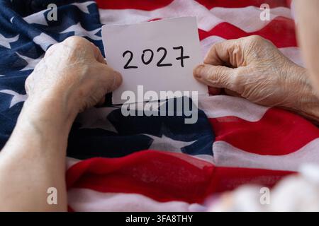 Une femme âgée tient une carte en papier portant le mot 2027 sur fond du drapeau américain, sur le thème du Nouvel An, du calendrier et de Holi Banque D'Images