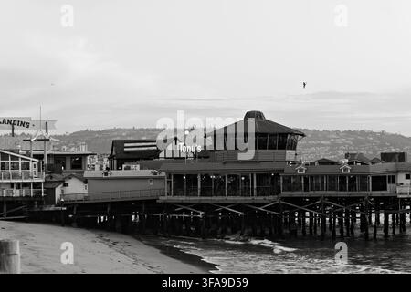 Une jetée en bord de mer s'étend dans une eau calme au crépuscule. Structure en bois avec toit de chaume et sièges en plein air. Les gens se promènent ou s'assoient, profitant d'une paisible s Banque D'Images