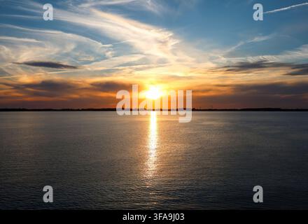 Le soleil plonge sous l'horizon, peignant le ciel de couleurs chaudes et se reflétant sur la surface paisible de l'eau Banque D'Images