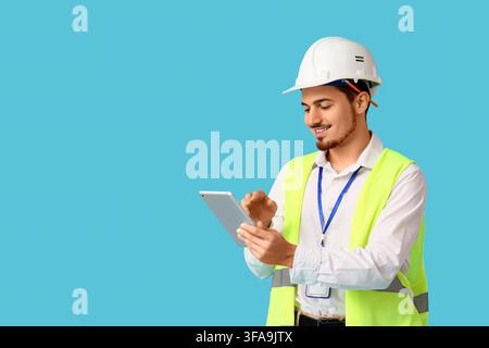 Technologie de construction et gestion de projet numérique, ingénieur souriant utilisant une tablette sur fond bleu Banque D'Images