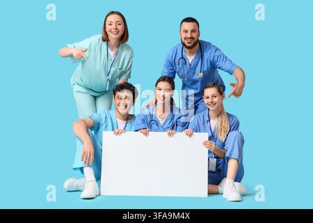 Équipe de soins de santé avec panneau vierge, professionnels médicaux et étudiants pointant vers l'espace de copie, groupe divers de médecins et infirmières Banque D'Images