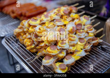 Un tas de brochettes de street food contenant des œufs de caille frits croustillants garnis de tranches de saucisse ou de hot-dog reposant sur un grille-pain métallique en extérieur Banque D'Images