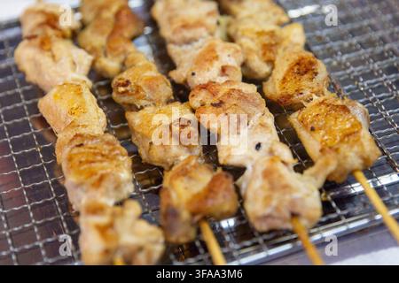 Rangées de brochettes de poulet grillées dorées ou bâtonnets de yakitori reposant sur une grille de refroidissement en acier inoxydable dans un stand de nourriture extérieur à Malacca, Malaisie Banque D'Images