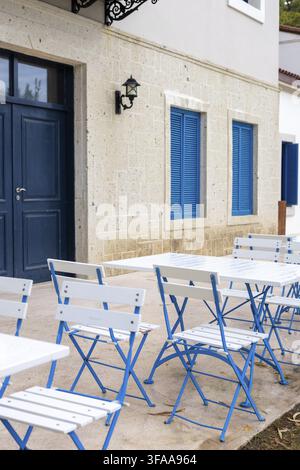 Tables et chaises bleues et blanches disposées soigneusement dans une salle à manger extérieure agrémentée de touches bleues et de meubles blancs. Parfait pour savourer un repas à l'extérieur Banque D'Images