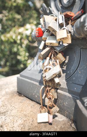 Une vue rapprochée de nombreux cadenas rouillés et neufs fixés à une structure métallique extérieure noire, illustrant la sécurité, la protection et les détails urbains wi Banque D'Images