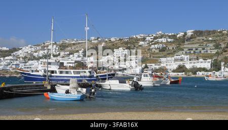 Vue d'un yacht à moteur bleu et blanc et de petits bateaux de pêche amarrés dans le port, avec des bâtiments blancs traditionnels sur la colline à Mykonos, en Grèce Banque D'Images